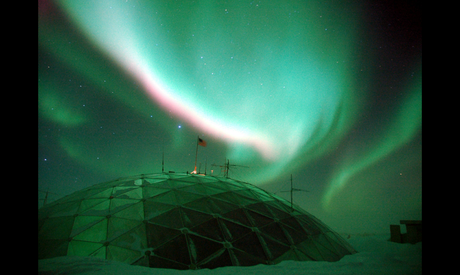 A picture of the aurora over top of a dome structure in the snow